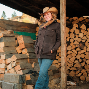 Cowgirl leaning against a pole wearing an oilskin jacket