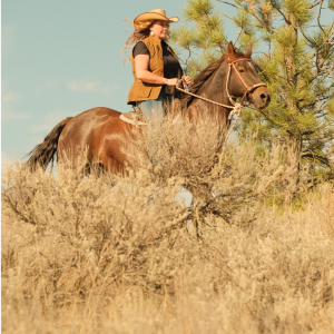 cowgirl riding horse in cowboy hat and oilskin vest