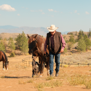 man in an oilskin vest leading a horse